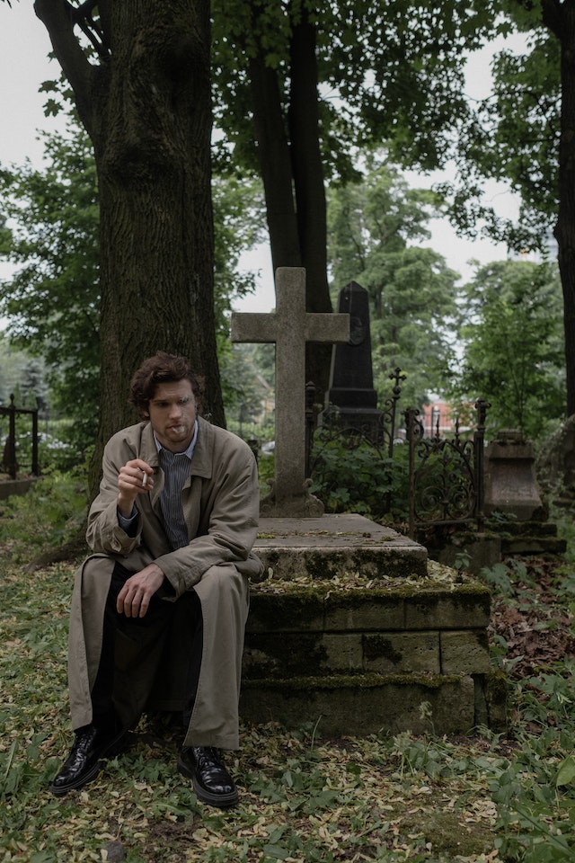Man sitting on a grave, smoking.